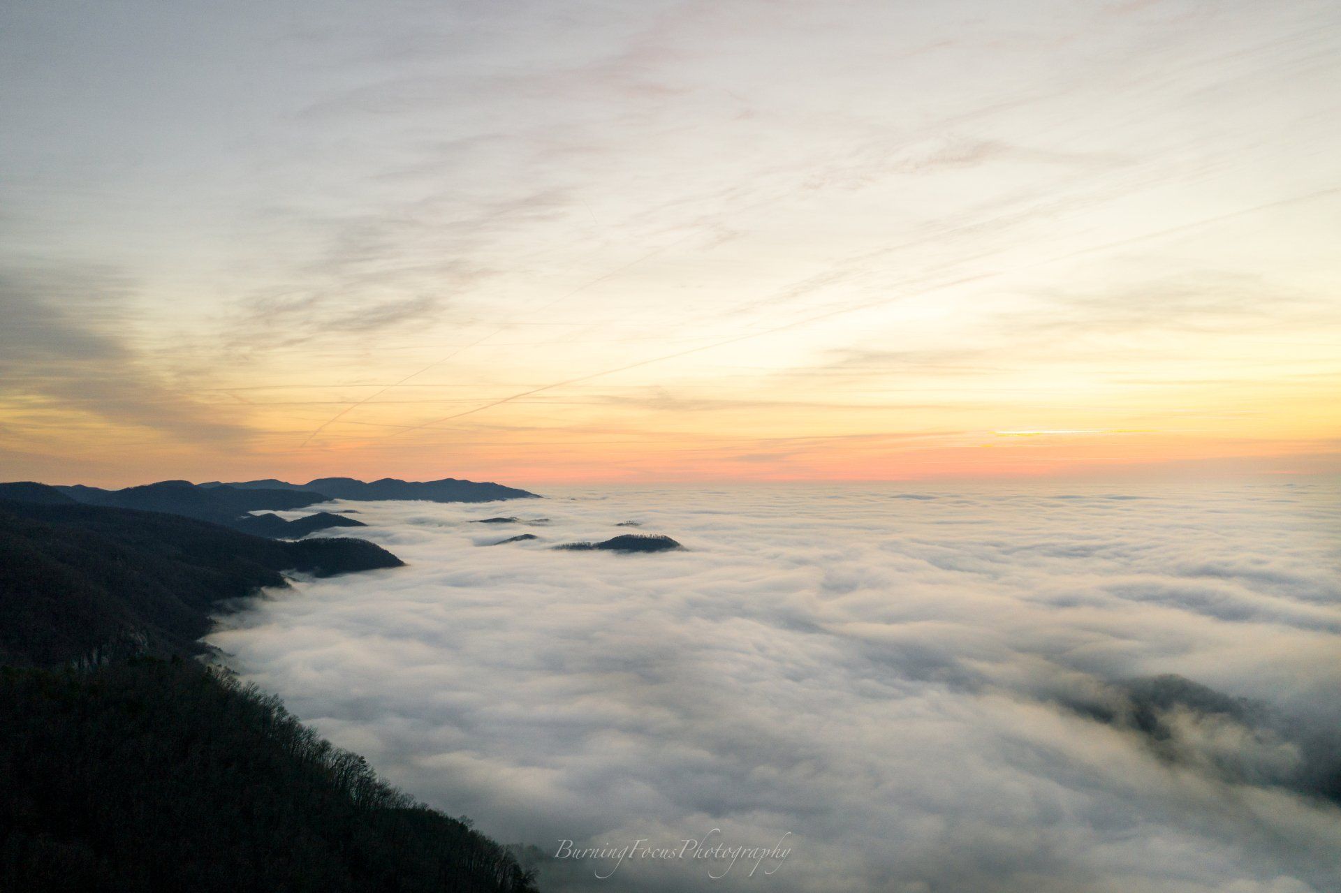 A view of a mountain covered in clouds at sunset