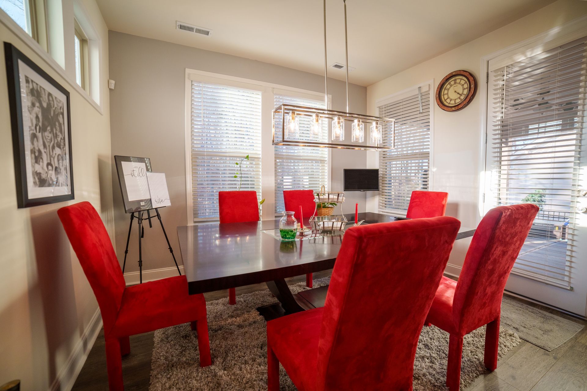 A dining room with a table and red chairs and a clock on the wall.