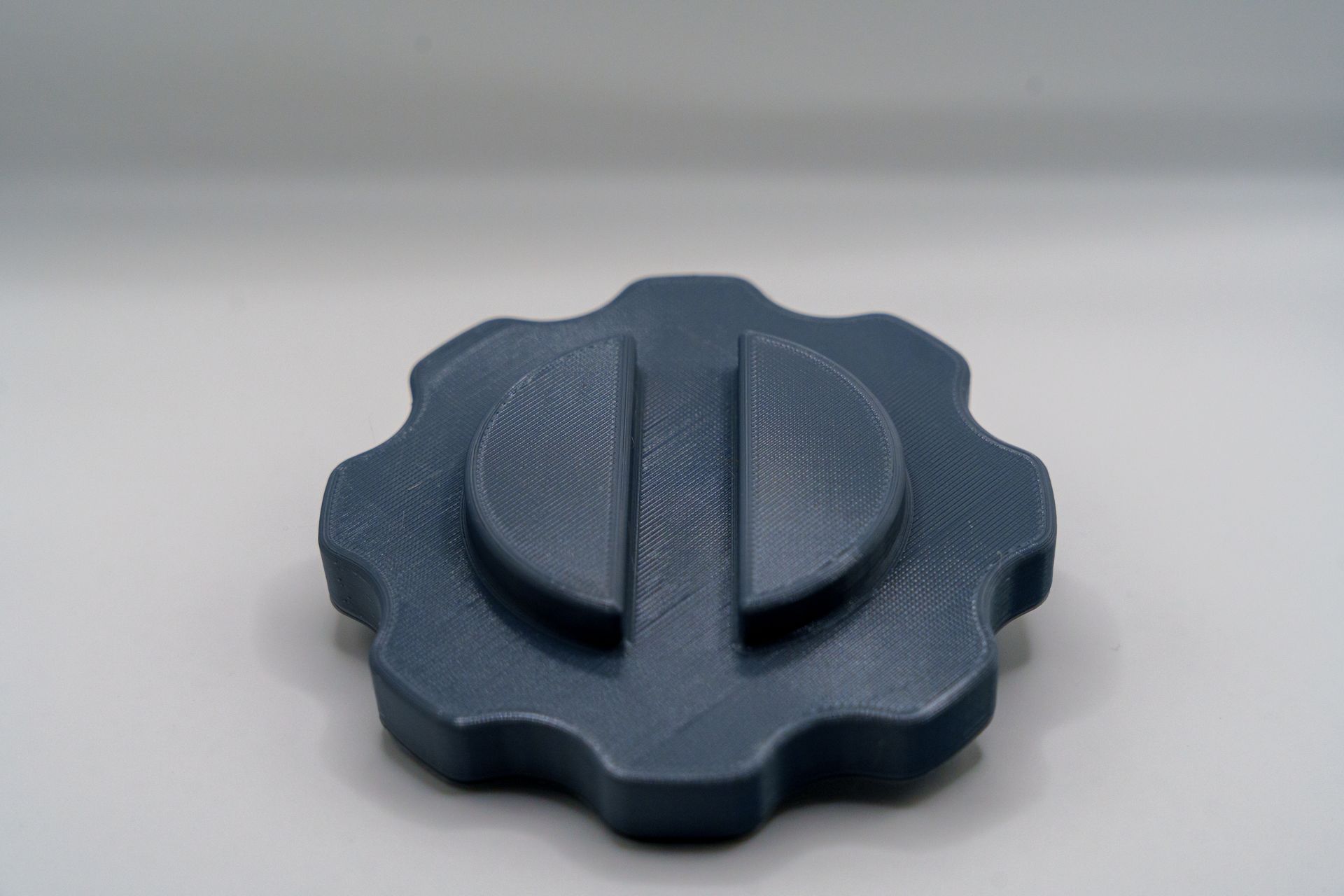 A black gear shaped object is sitting on a white surface.