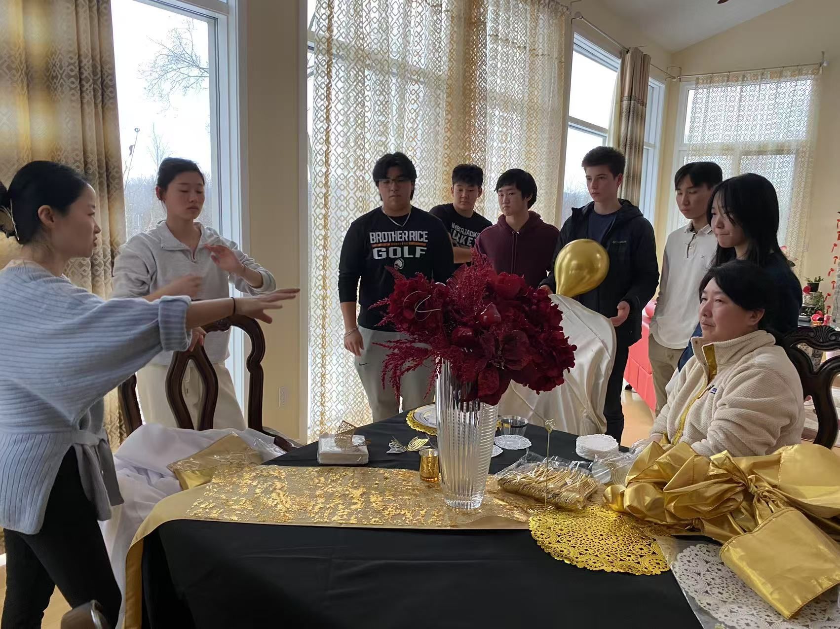 Group of people around a table with decorations, including a seated woman and someone gesturing.