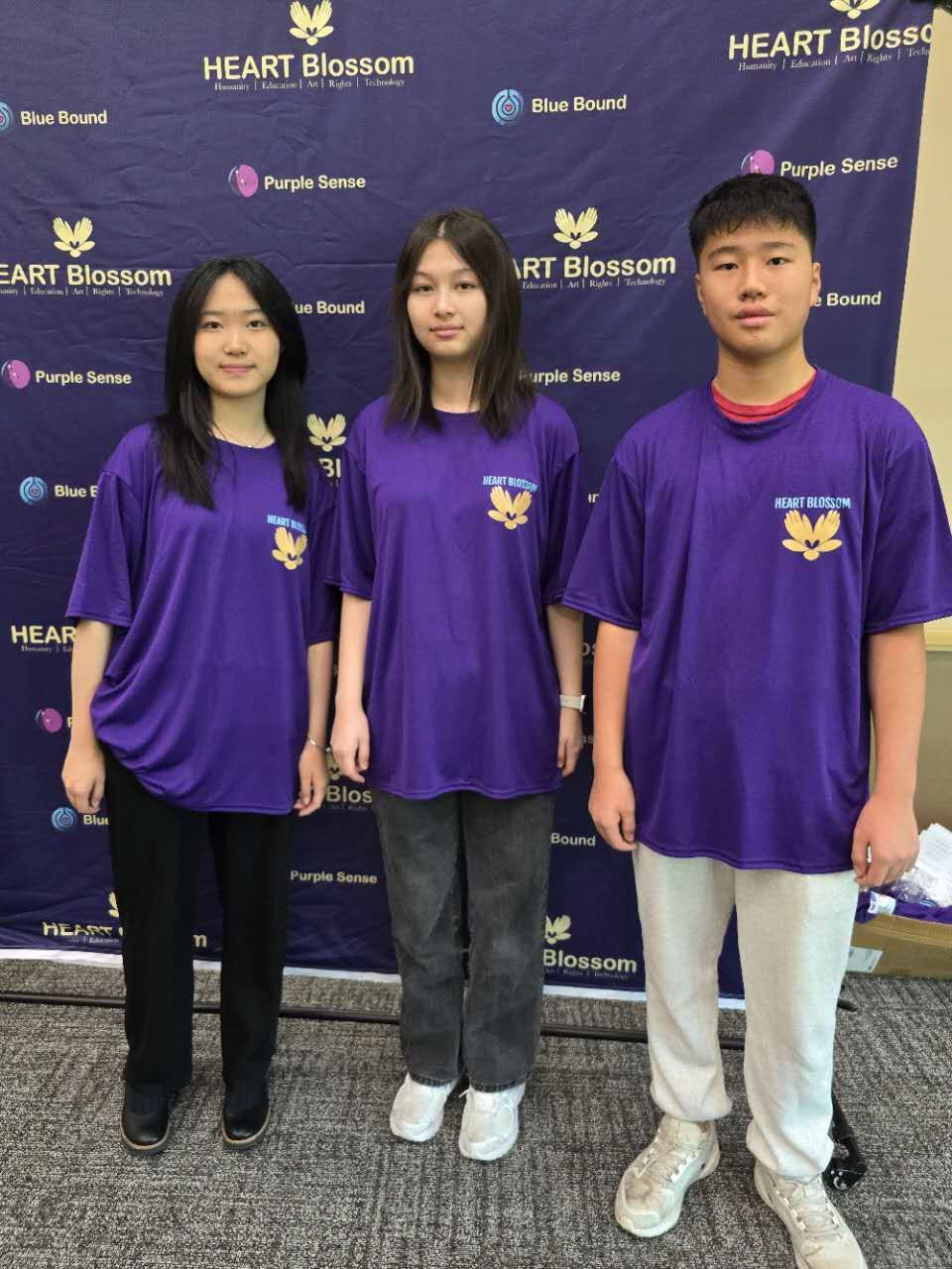 Three young people wearing purple shirts stand together.