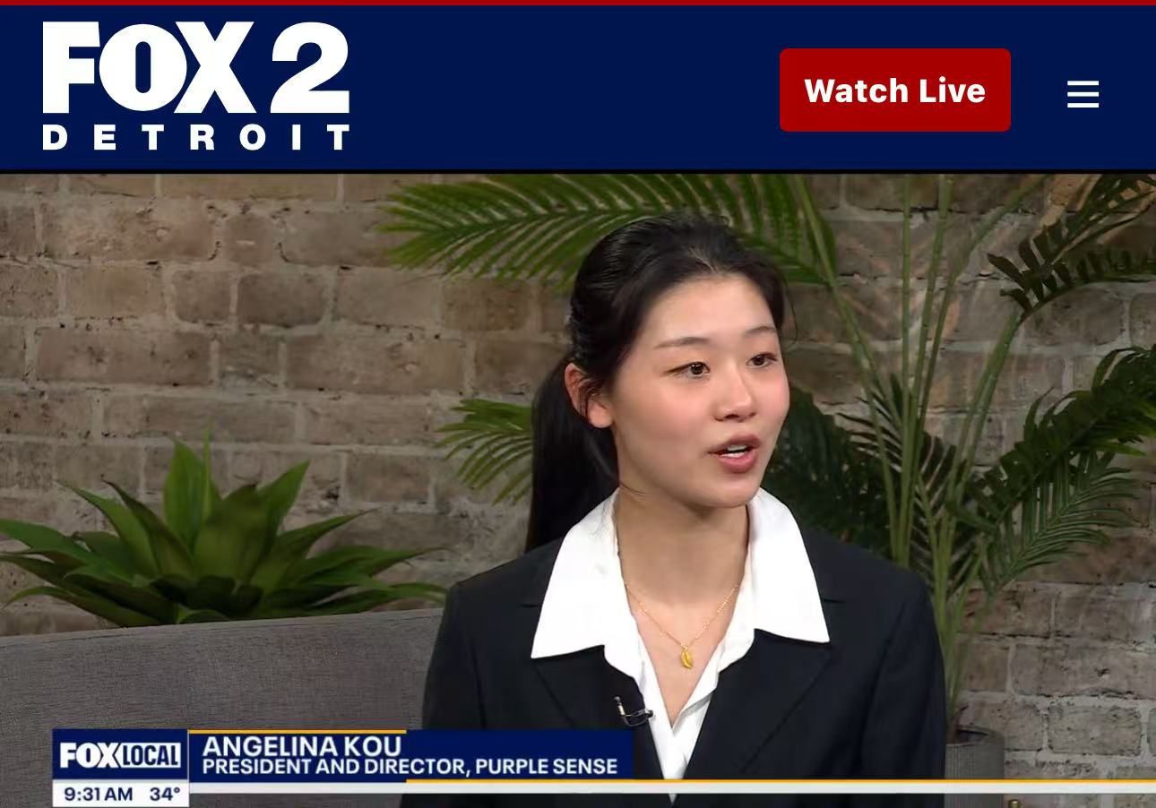 Angelina Kou speaking on Fox 2 Detroit. She is wearing a blazer and standing in front of a brick wall.