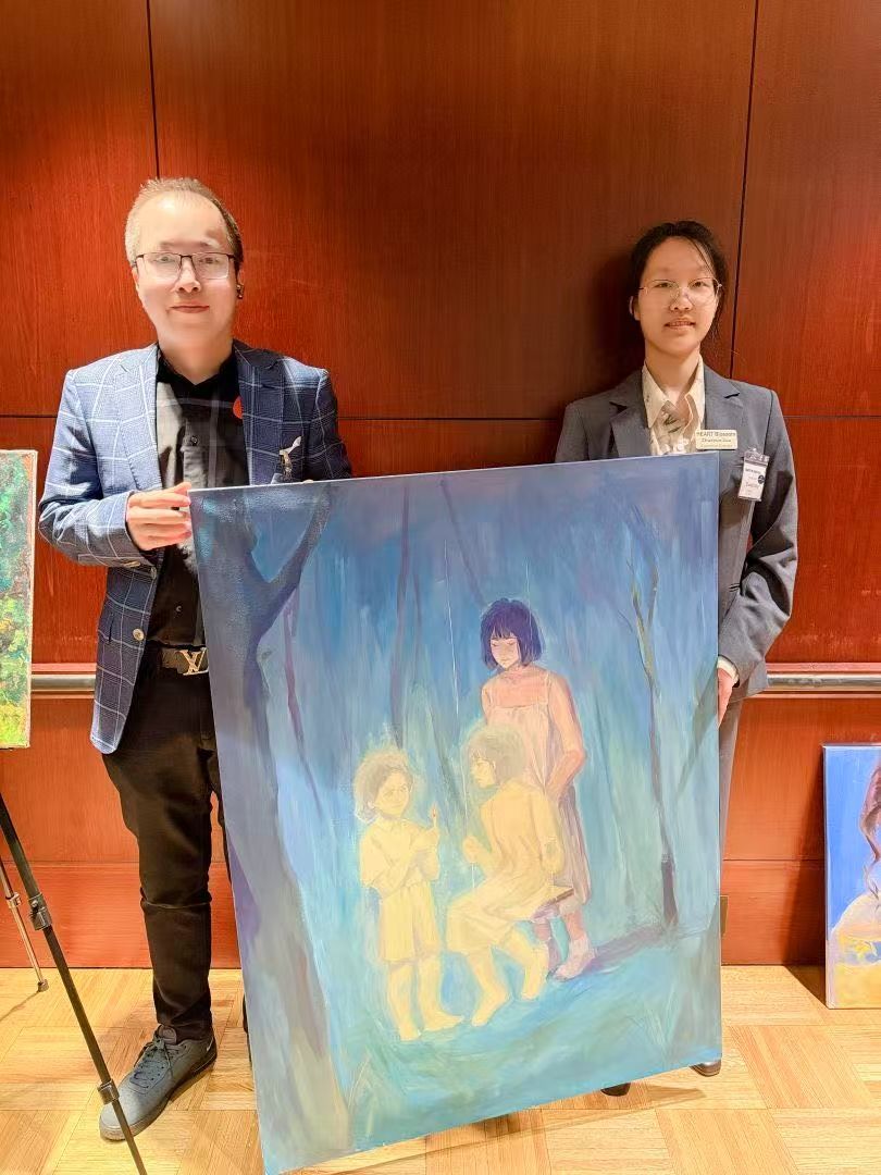 Two people holding a painting of children on a swing, against a blue-green background.