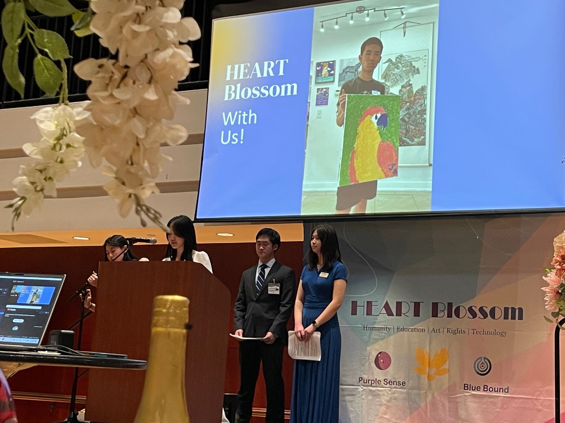 People on stage at an event with a screen showing art. 