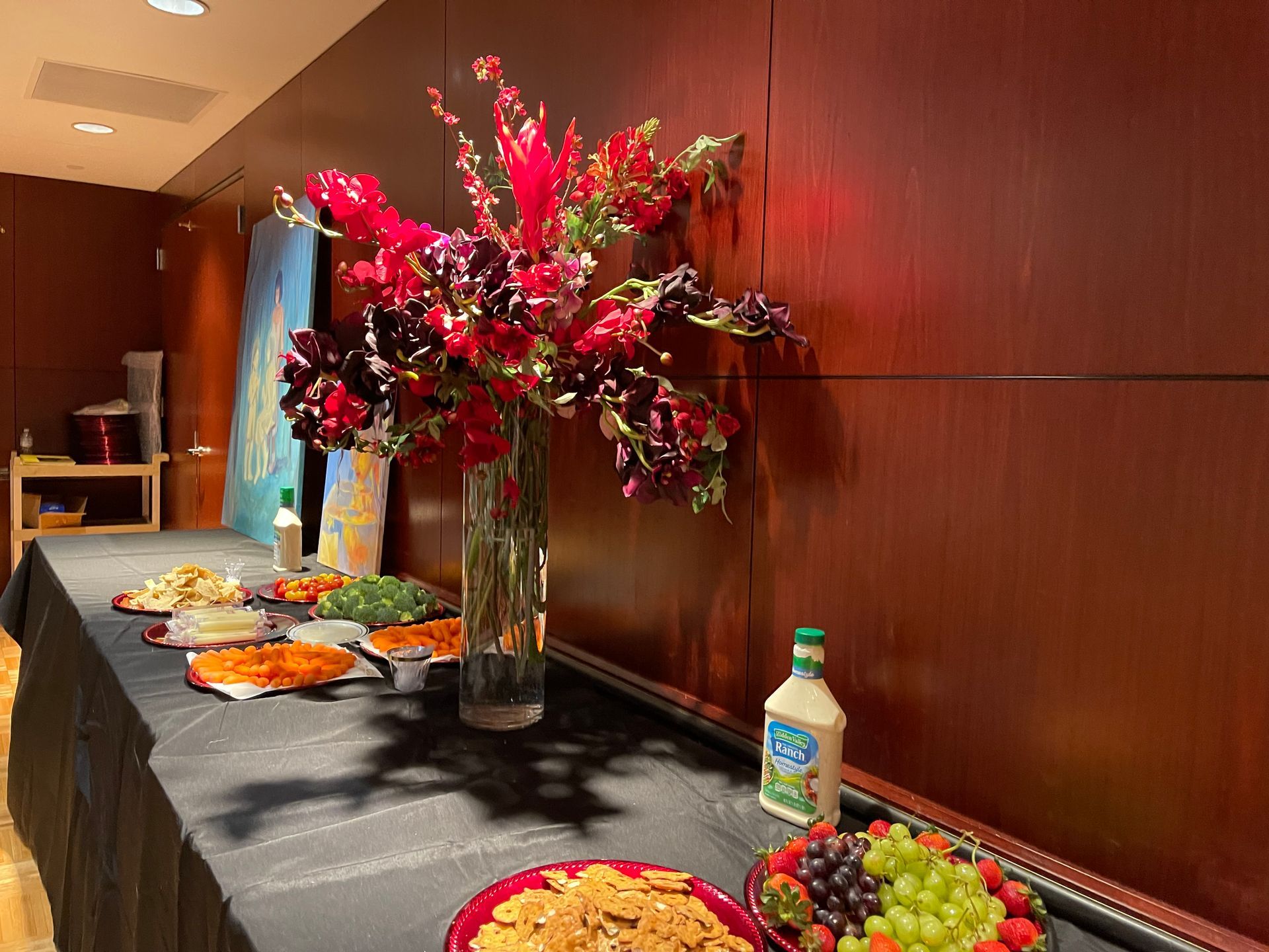 Buffet table with a large floral arrangement, various food dishes, and a bottle of ranch dressing.