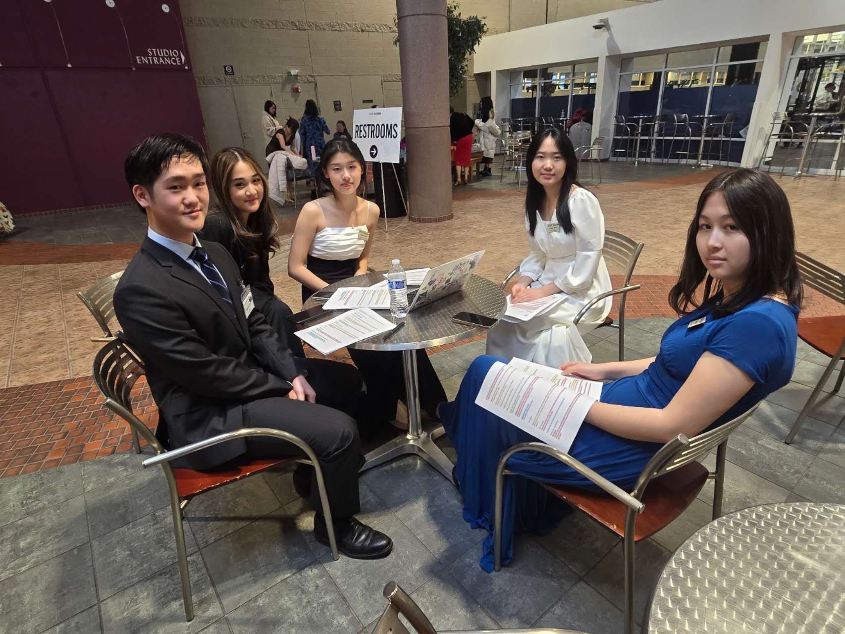 Five formally dressed people at a table: a man and four women, likely at an event, indoors.