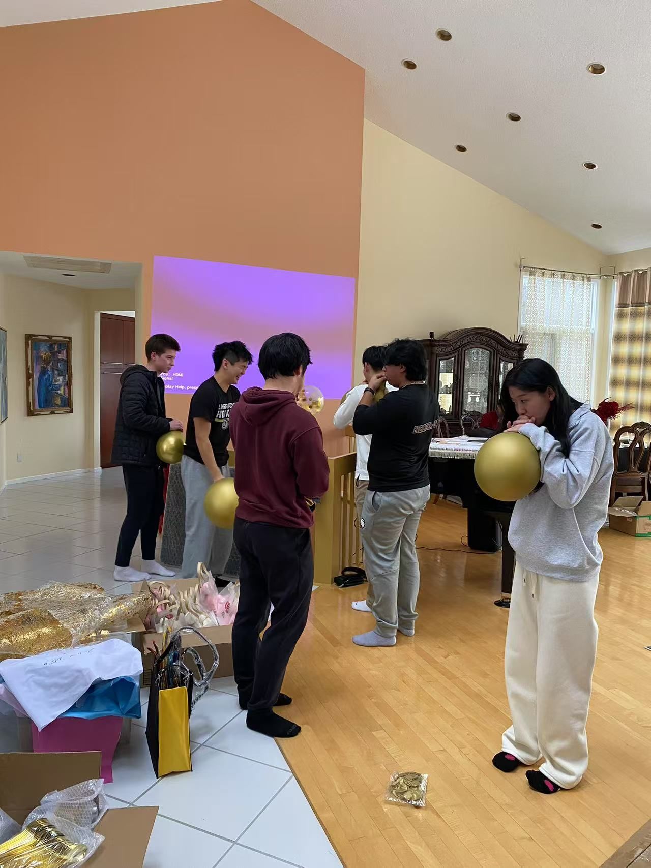 Group of young people blowing up gold balloons in a brightly lit living room.