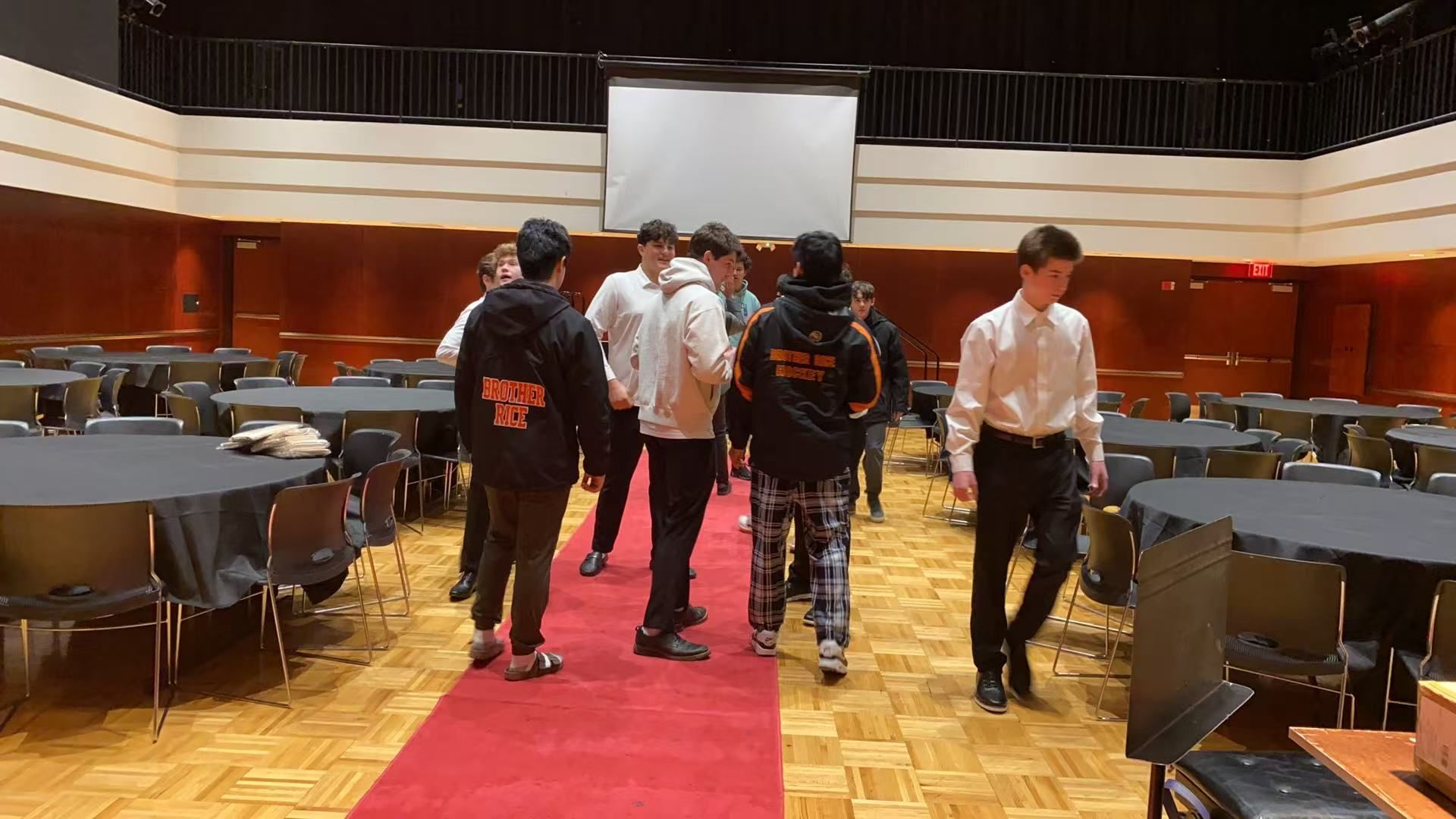 A group of young men walk down a red carpet in a banquet hall.
