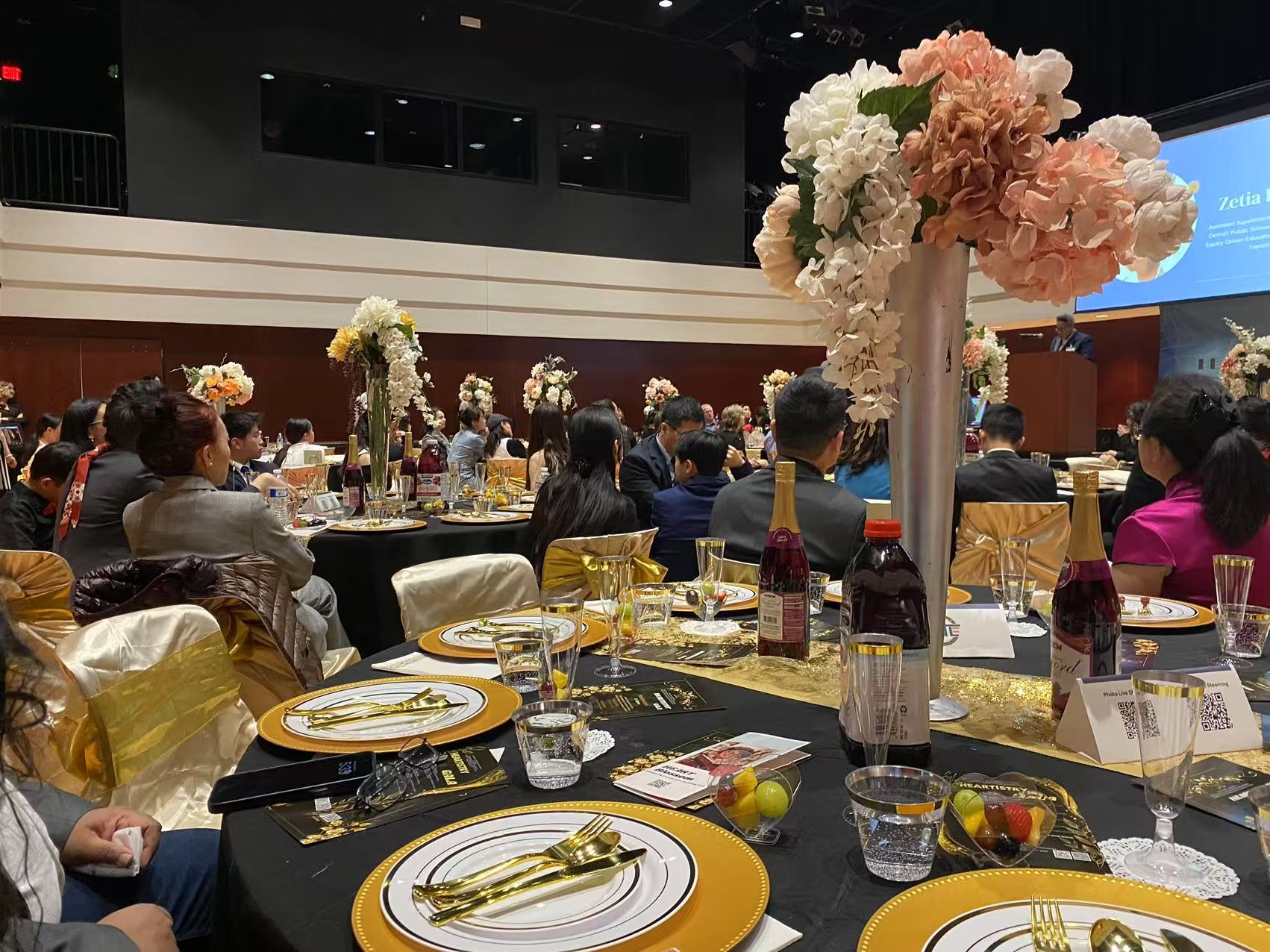 Elegant banquet hall with tables set for a formal event, floral centerpieces, and people seated.