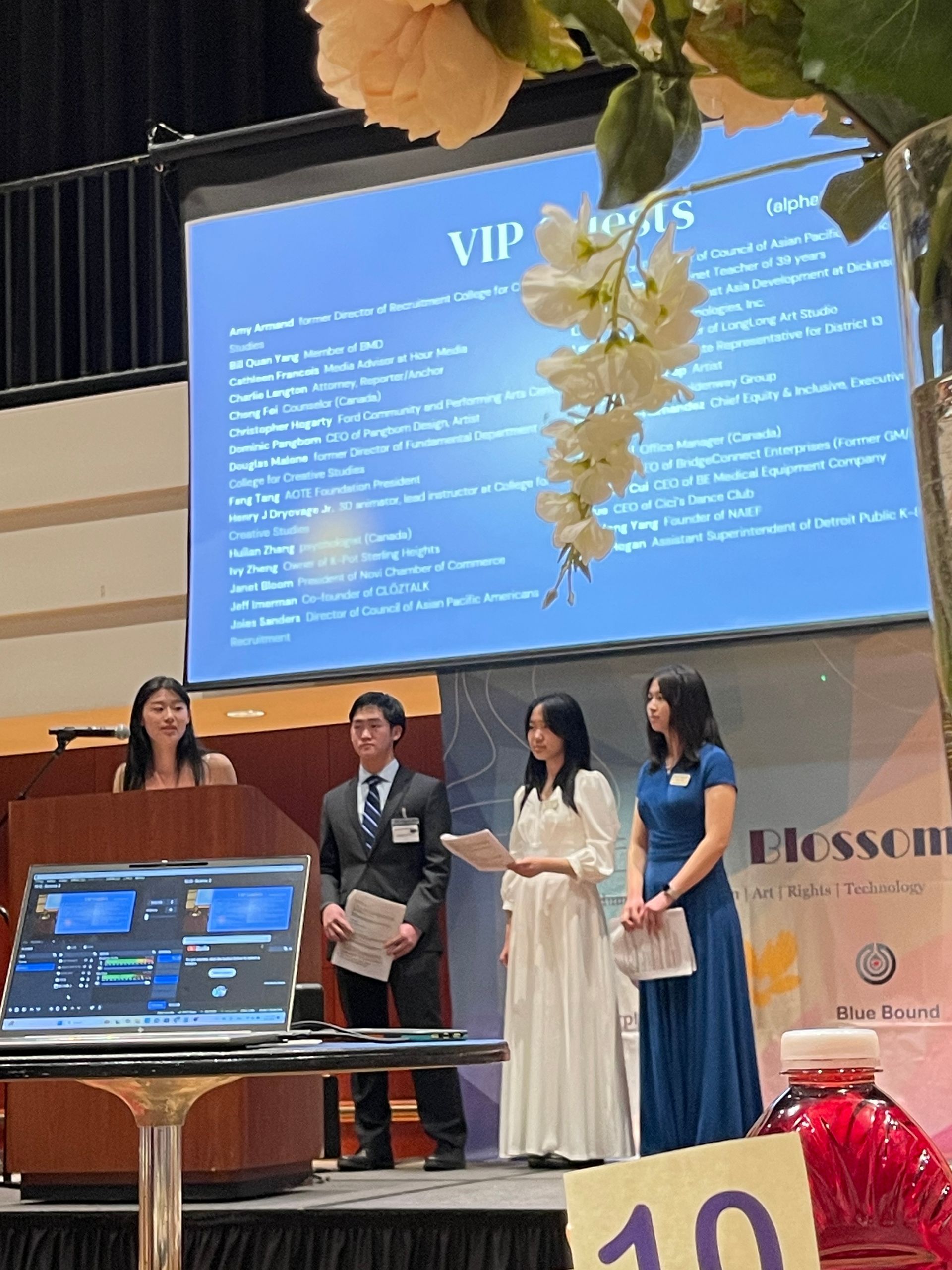 Four students present at an event, with a screen behind them listing VIP guests.