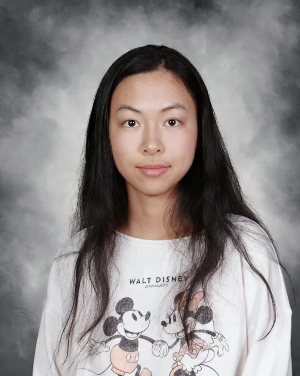 Woman with glasses smiles outdoors near blossoming tree.