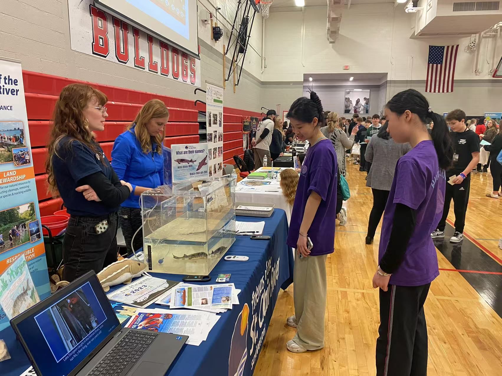 Two women at a table with students looking at an aquarium in a gymnasium.