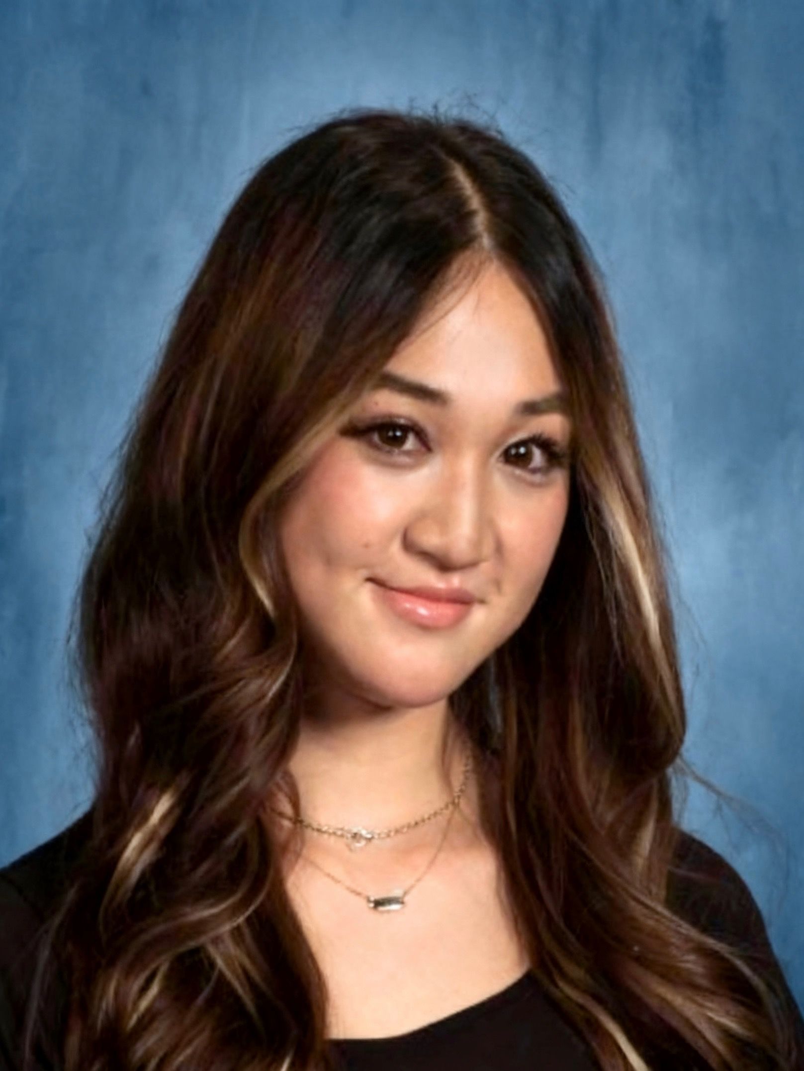 Woman with glasses smiles outdoors near blossoming tree.