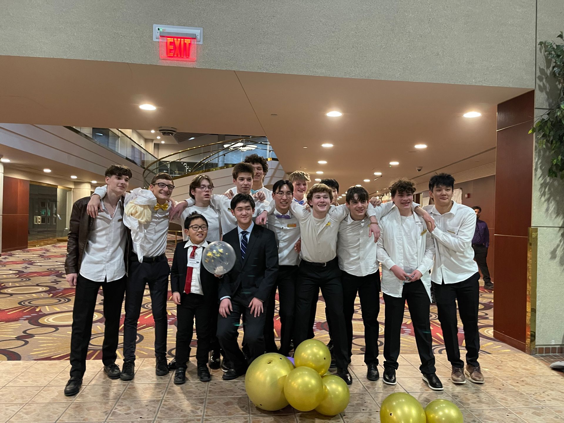 Group of young men in formal attire pose with balloons indoors.