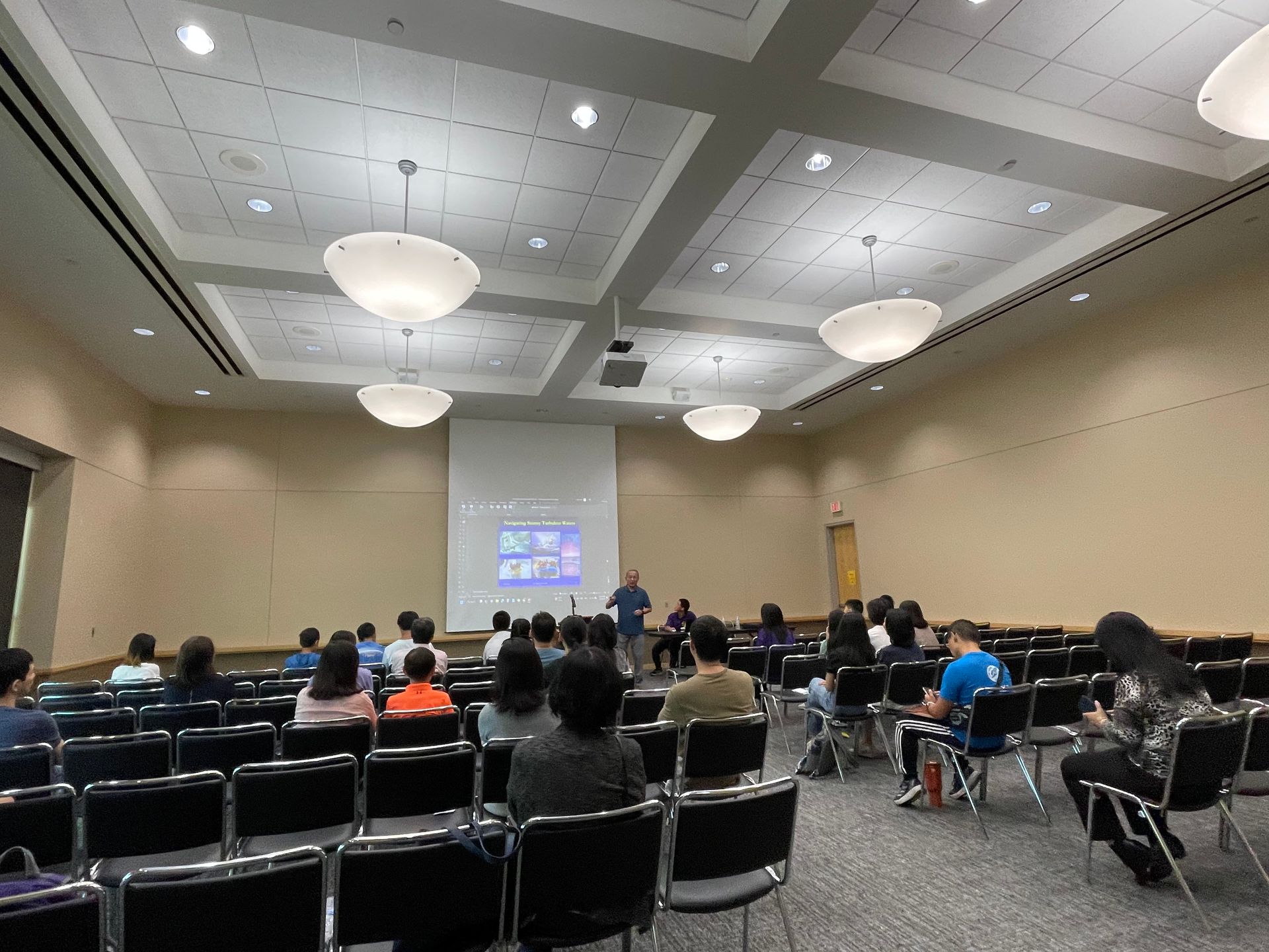 People seated in rows, attending a presentation in a large conference room.