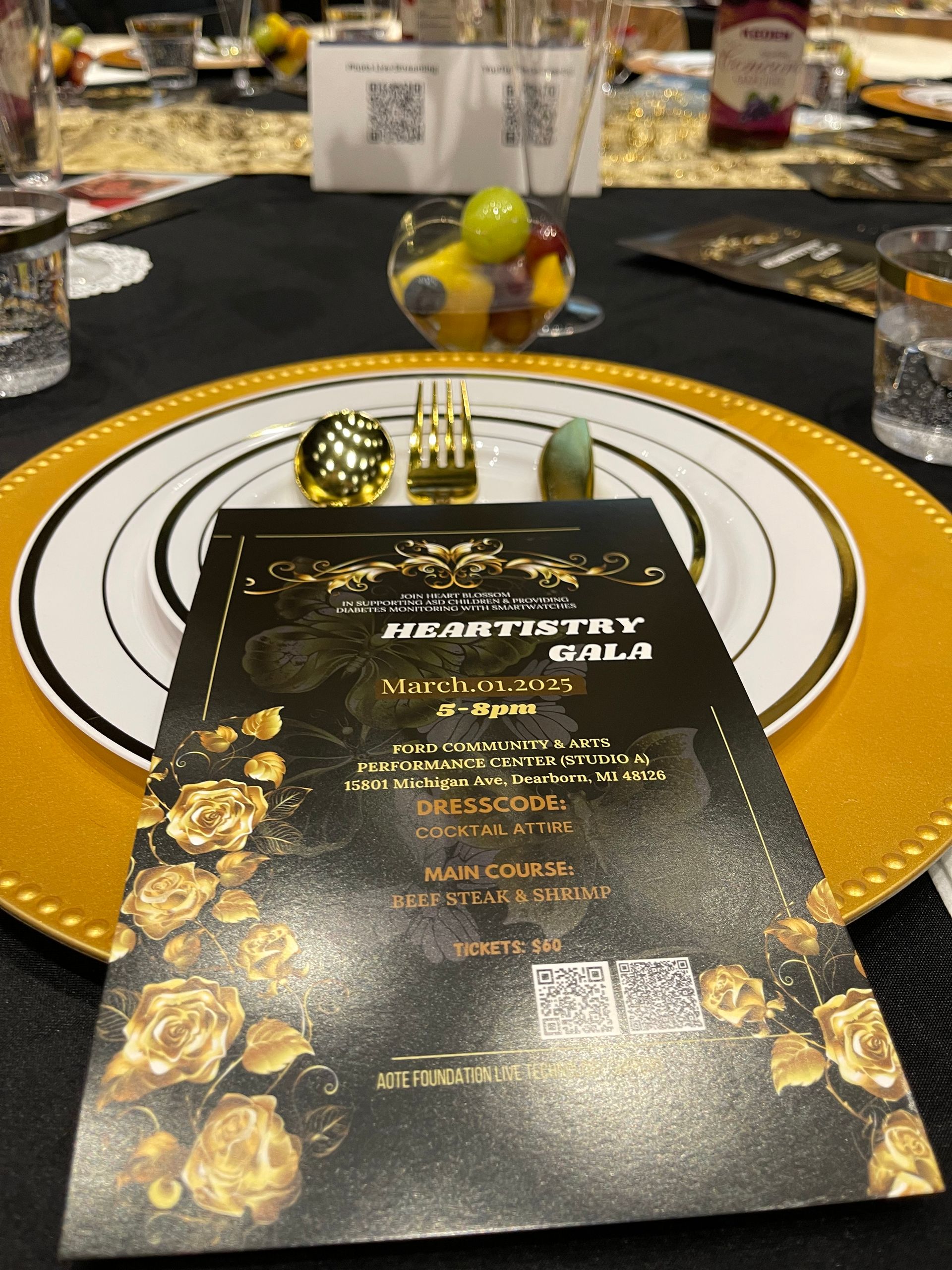 Place setting at a gala with a gold, black and white color scheme, fruit bowl, and invitation.