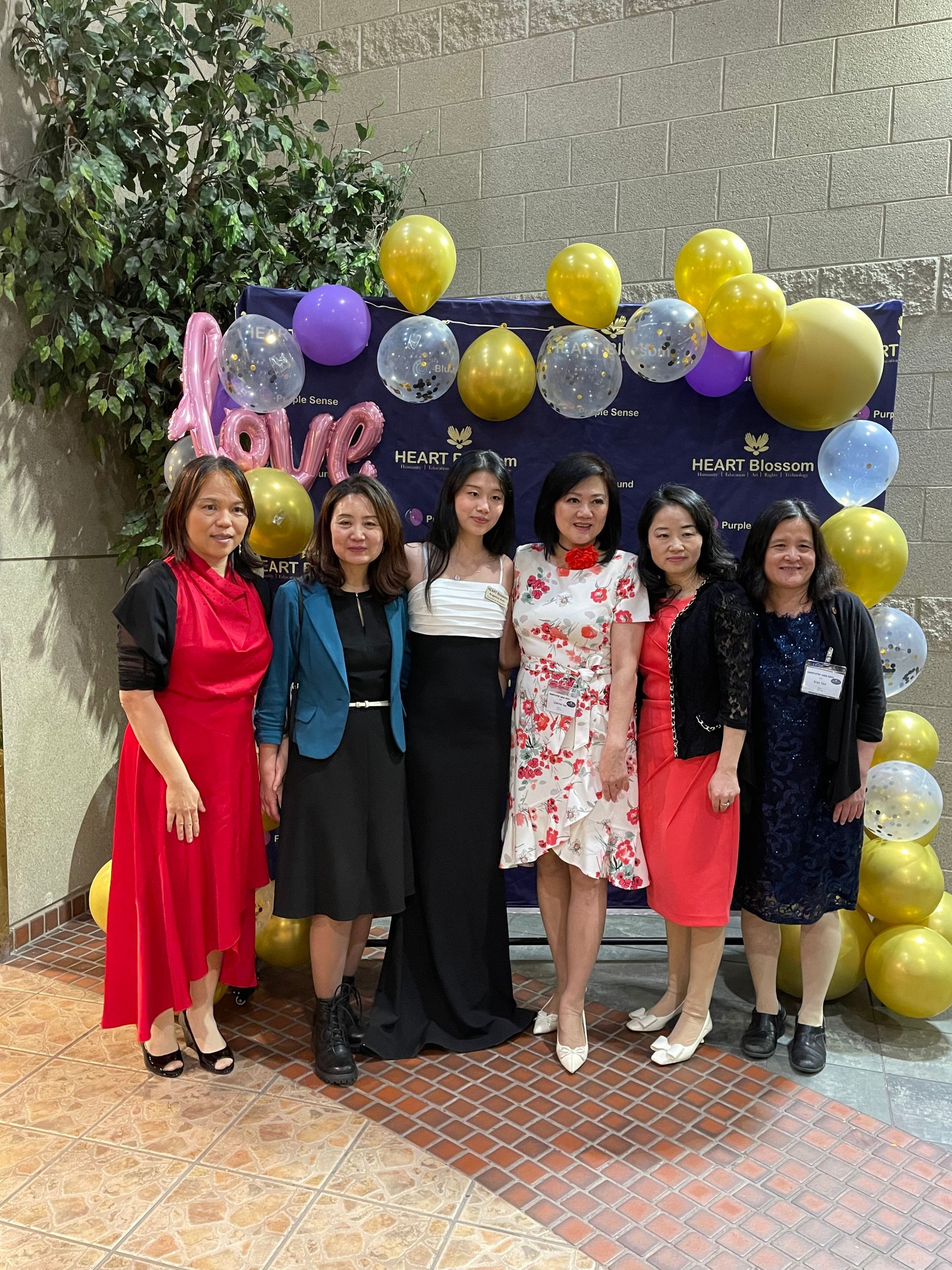 Group of six women posing in front of a backdrop with balloons.