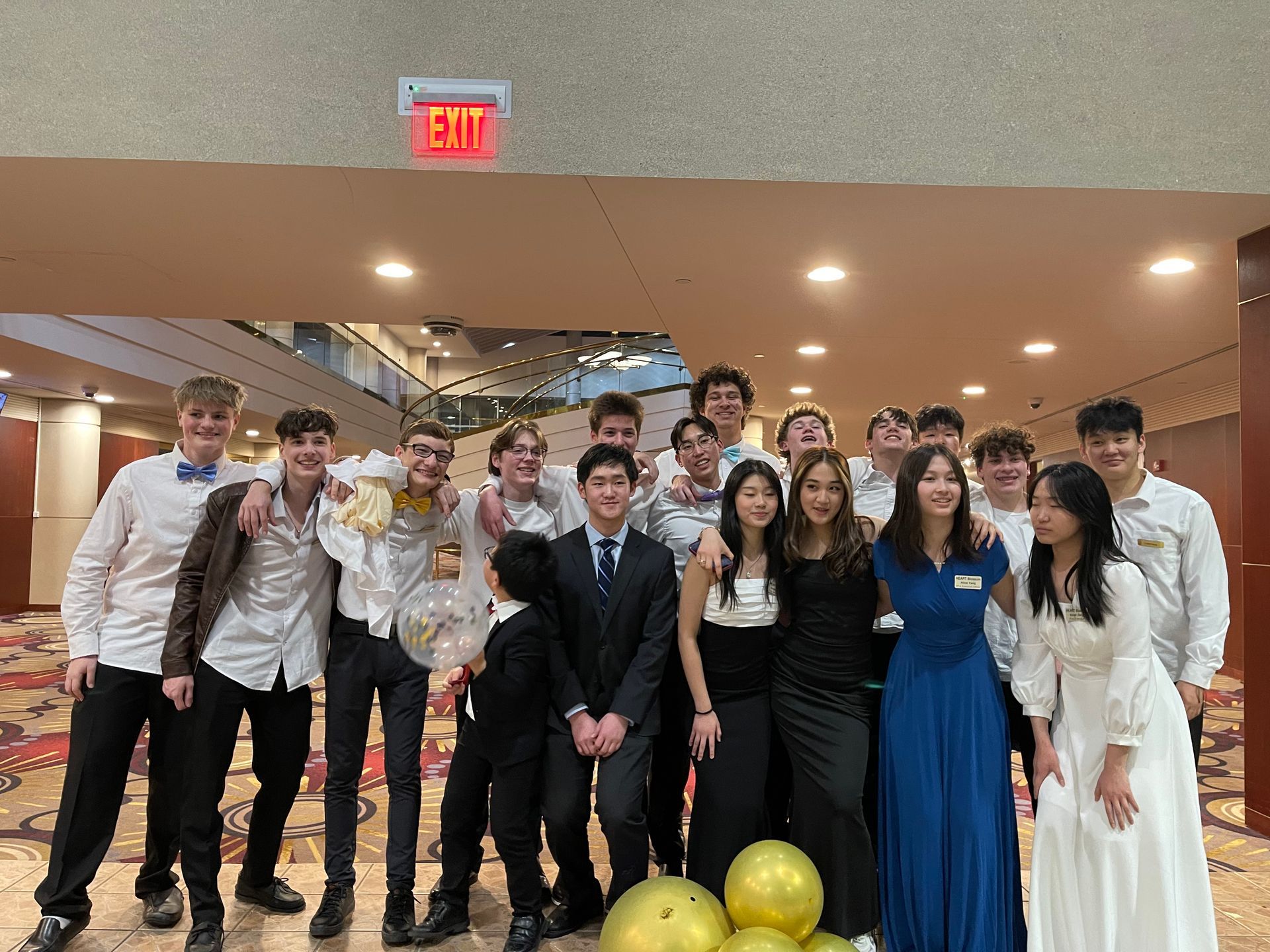 Group of young people in formal attire posing in a large building with an exit sign.