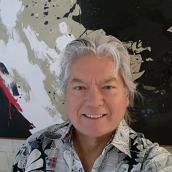 Man with gray hair smiles, posing in front of abstract art; wearing patterned shirt.