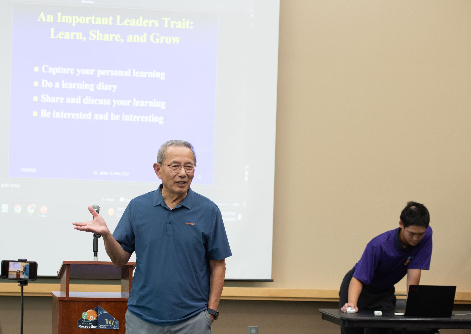 Man in  presentation, gesturing with left hand. Slide titled 