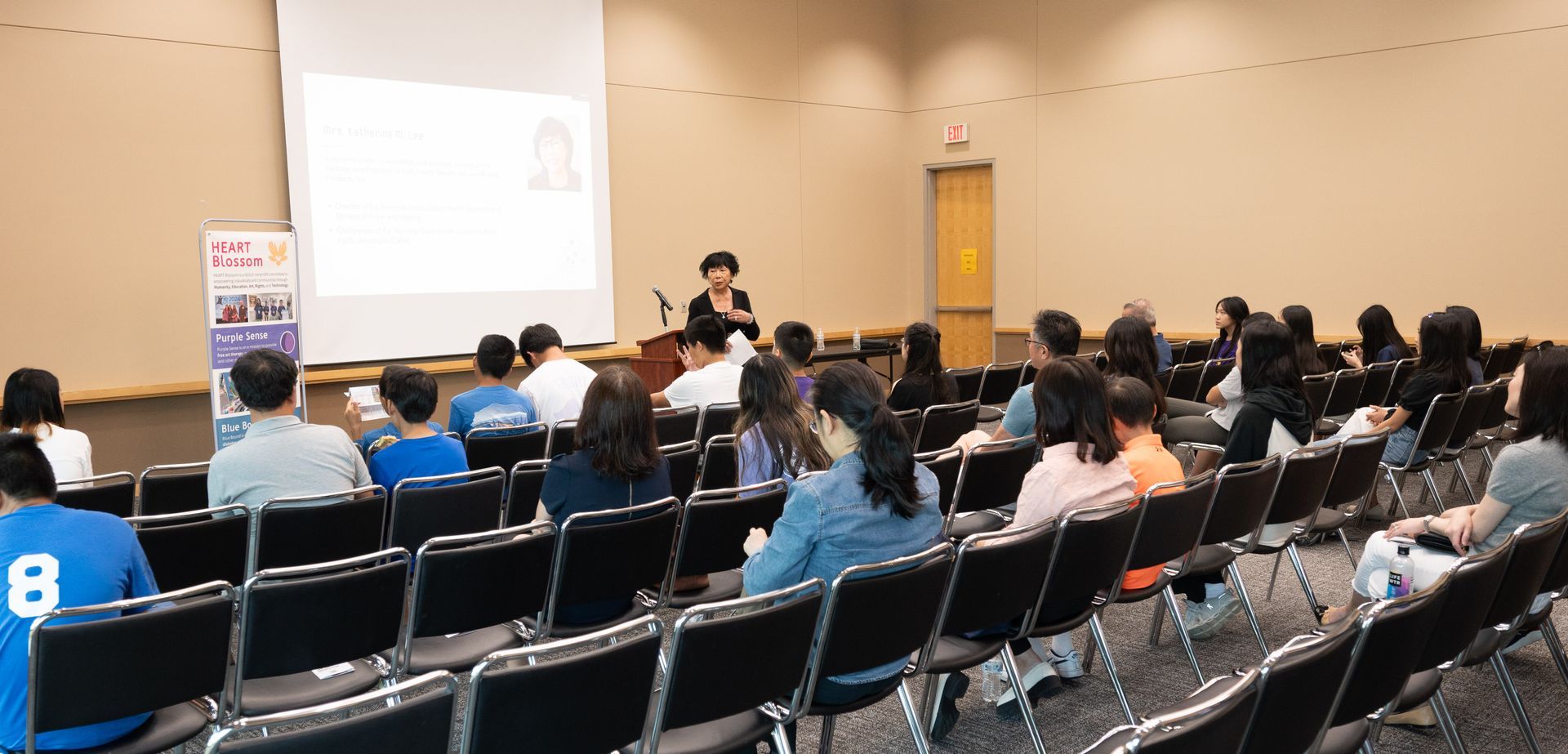 A presenter giving a lecture in a conference room, with an audience seated in rows of chairs.