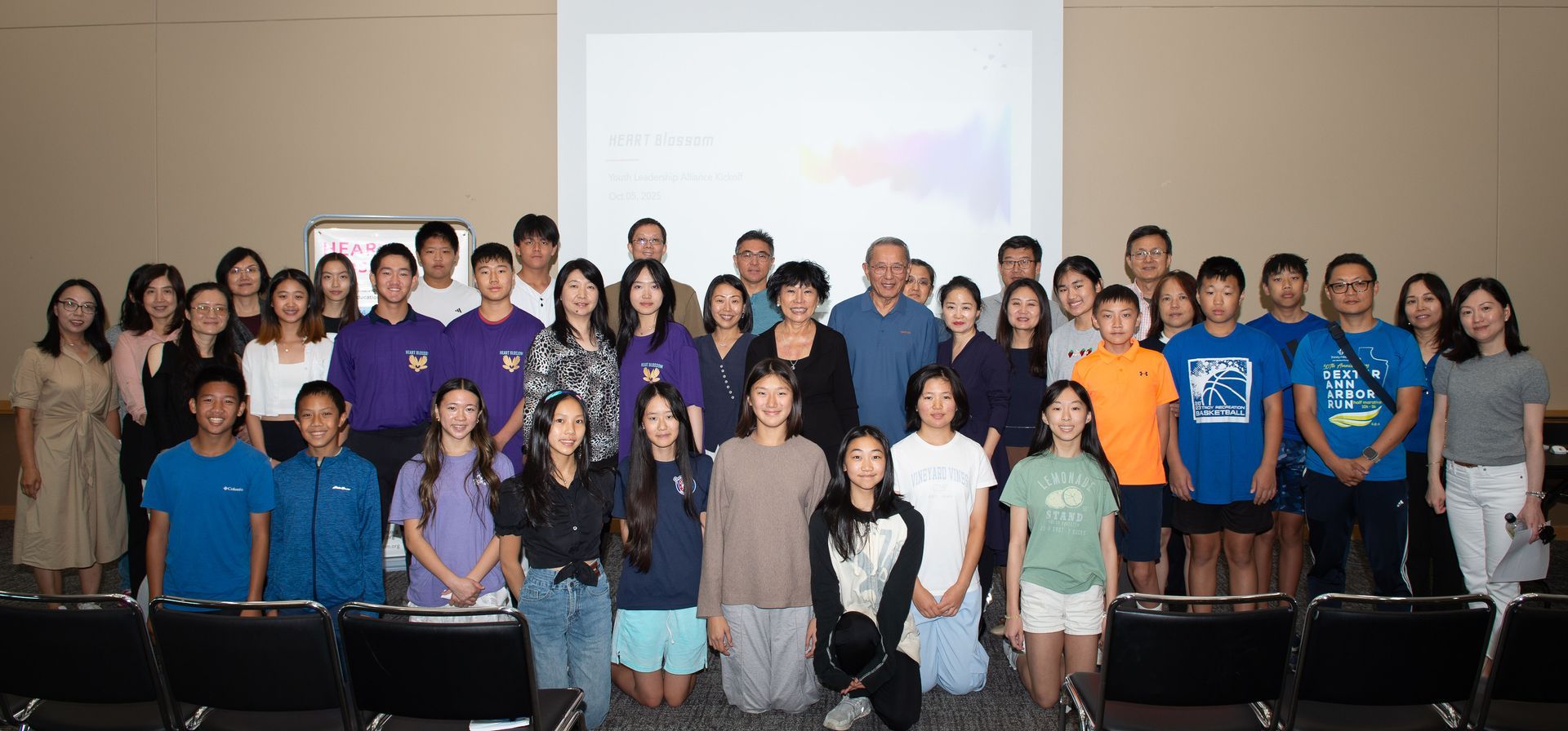 Group photo of diverse people in front of a projection screen, smiling at the camera in a conference room.