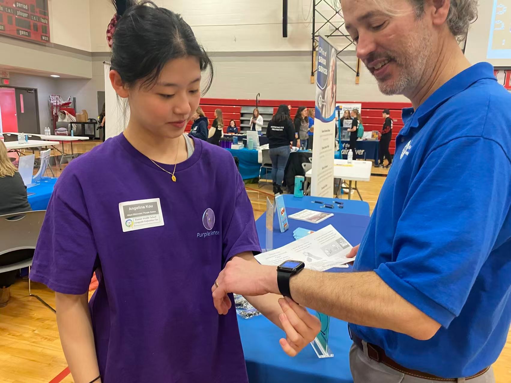 A man in blue shirt examines a woman's wrist with a watch at a health fair.
