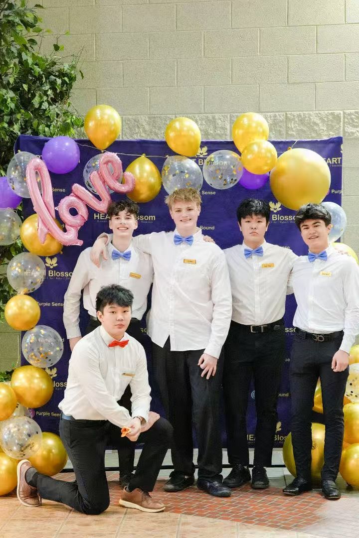 Group of young men posing in front of balloons. Some wearing bow ties and white shirts, the word 
