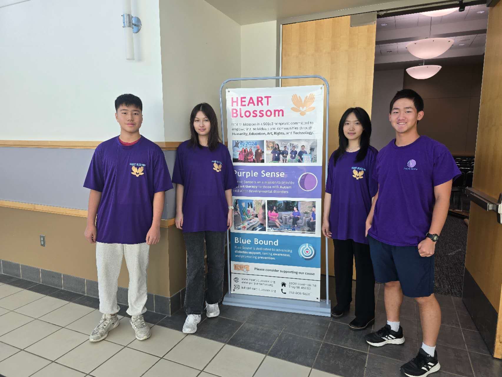 Four people in purple shirts stand by a banner. They're inside a building, likely promoting 