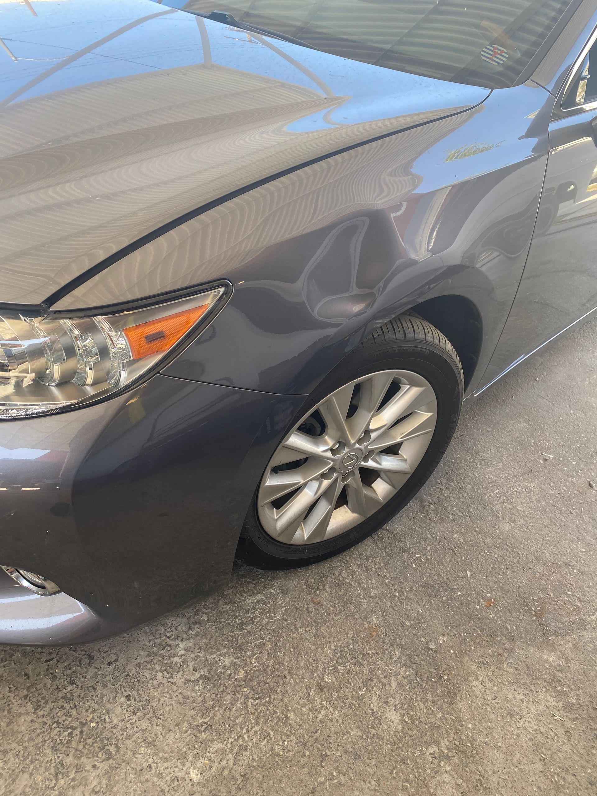 A gray car with a damaged fender is parked on the side of the road.