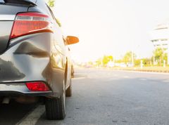 A car with a damaged bumper is parked on the side of the road.