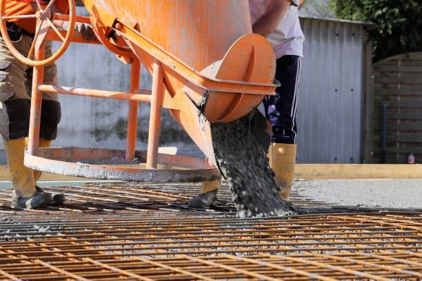 Workers pouring ready-mix concrete over steel reinforcement at a construction site.