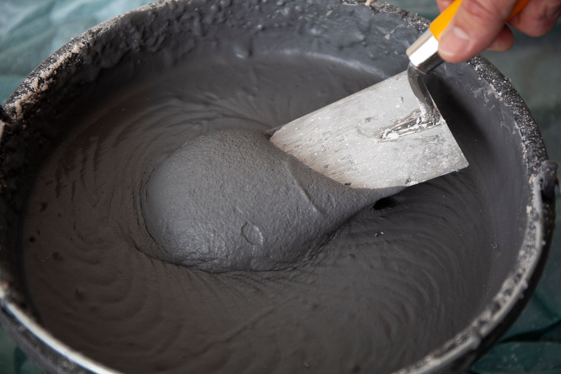 Hand of a worker with a trowel in a bucket with concrete plaster.