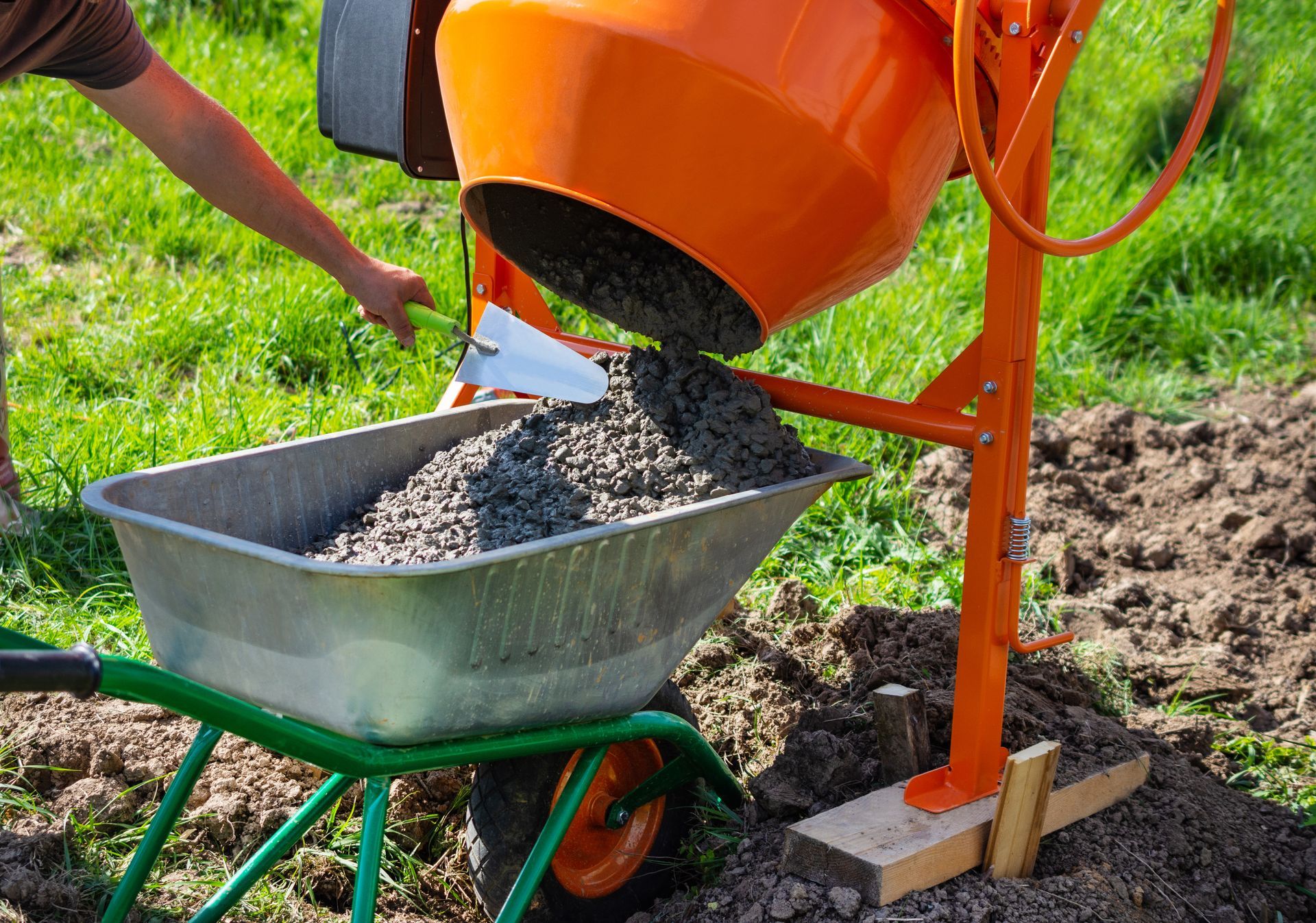 Concrete mix is being poured out of an orange concrete mixer, into a silver cart.