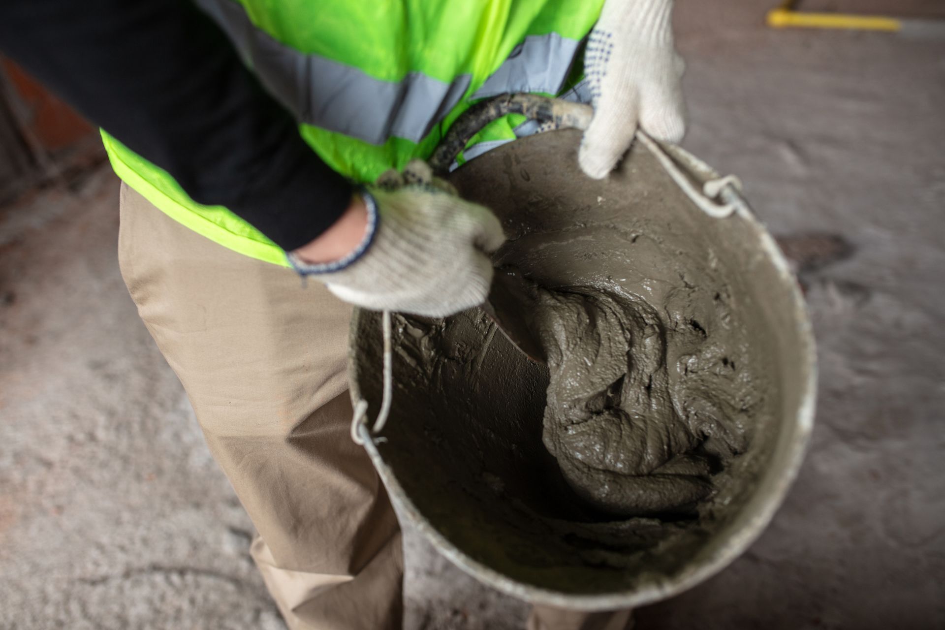 A construction worker handles a concrete mix inside a bucket on a construction site.