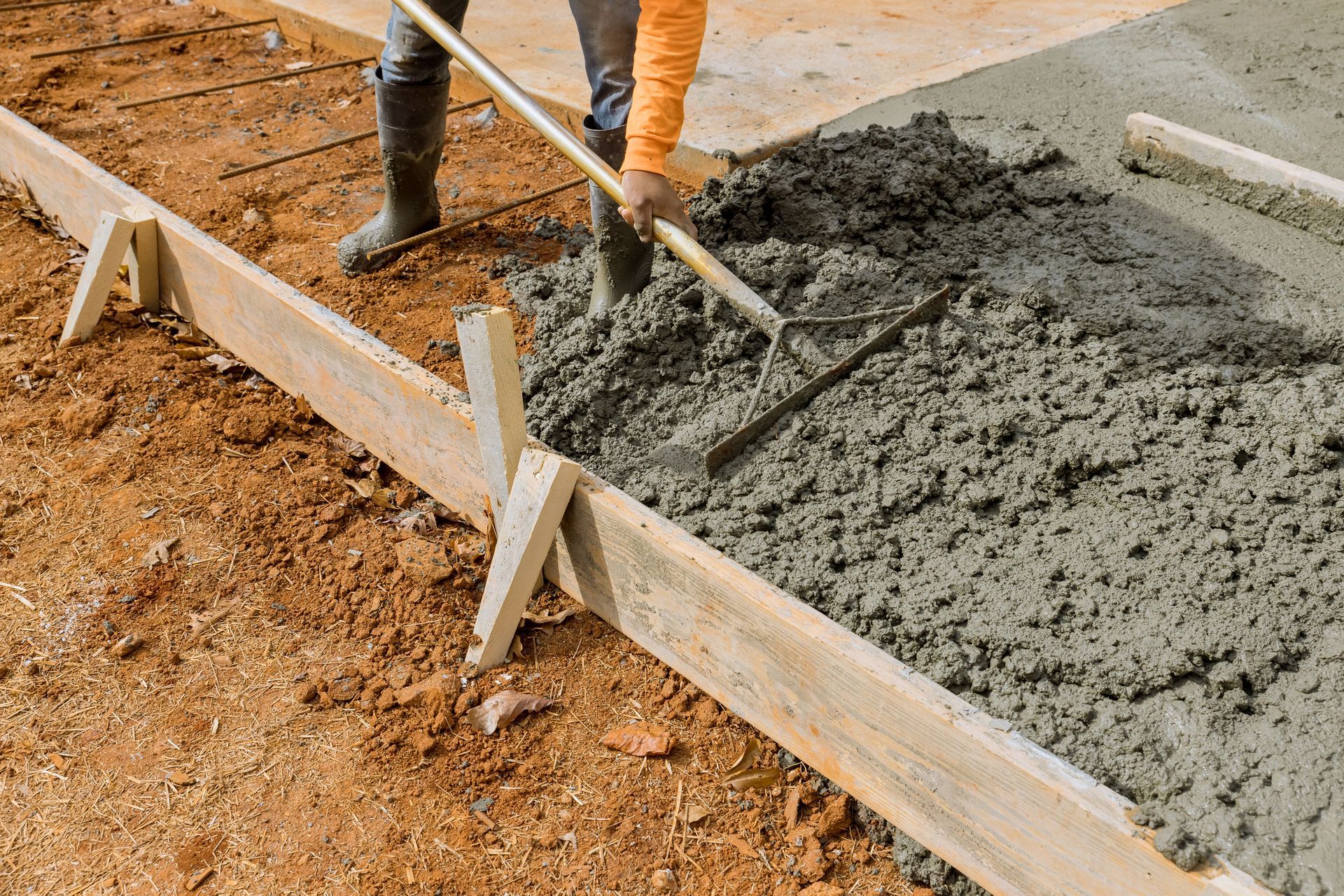 Workers pouring concrete, showcasing ready mix cement for a new sidewalk beside house.