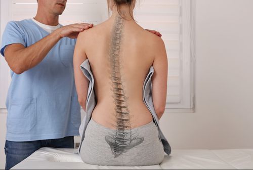 A woman is sitting on a table while a man examines her spine.