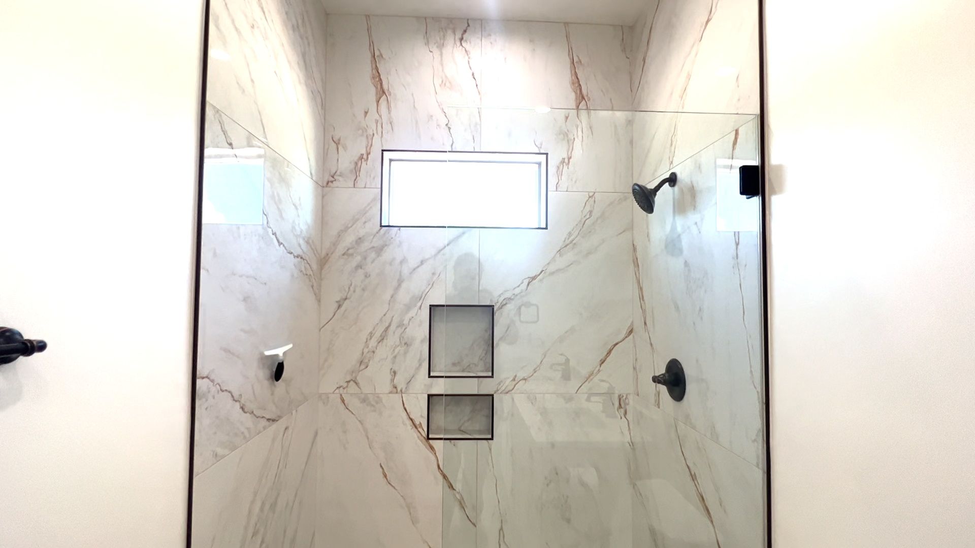 A bathroom with marble walls and a walk in shower with a glass door.