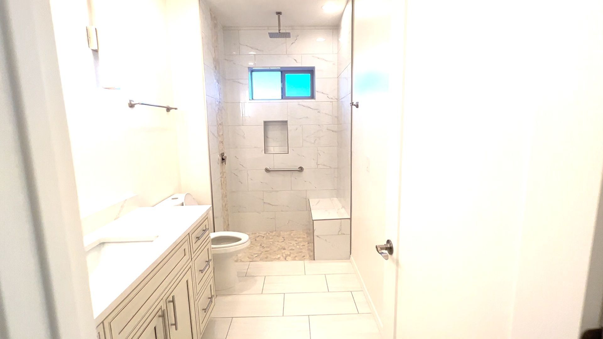A bathroom with a walk in shower , sink , toilet and window.