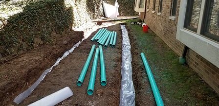 A bunch of green pipes are laying on the ground in front of a house.