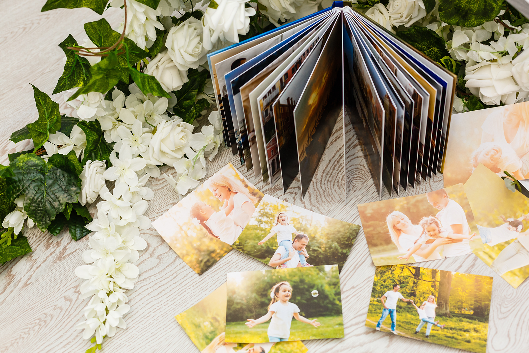 Photo album and loose photos of a family, displayed on a white surface with flowers.