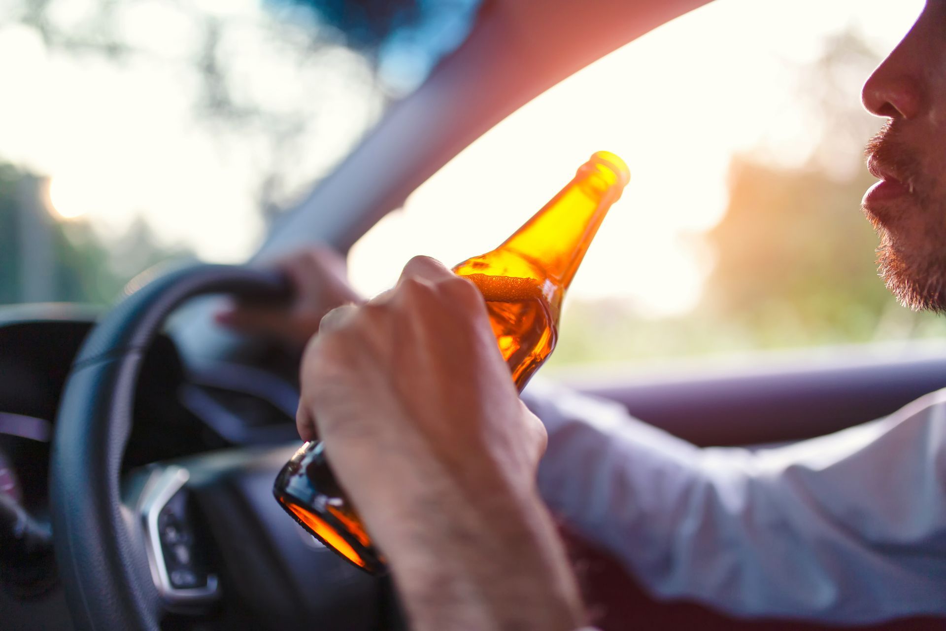 A man is holding a bottle of beer while driving a car.