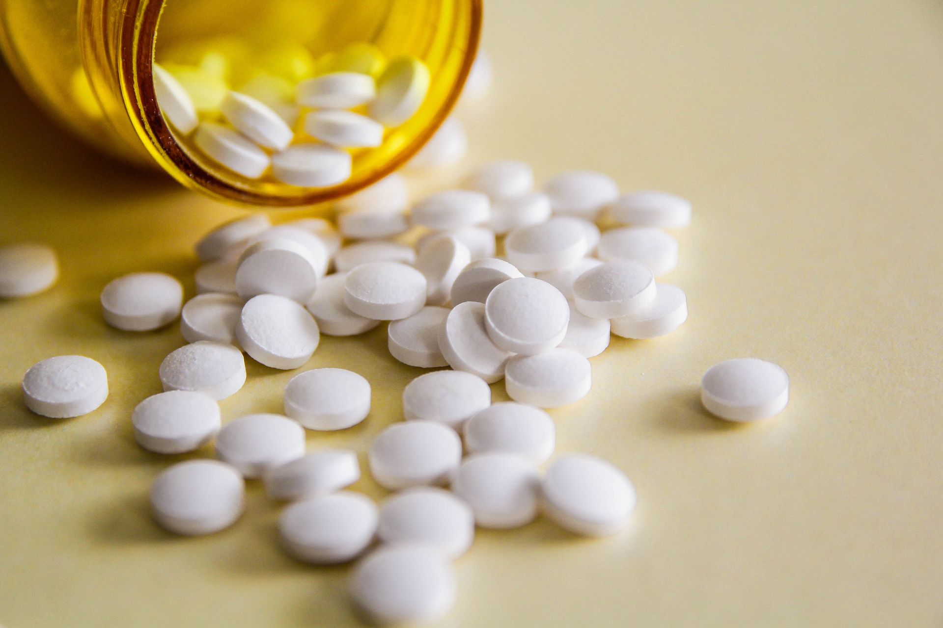 A bottle of pills is pouring out of it on a table.