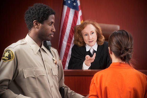 A woman in an orange prison uniform is talking to a judge in a courtroom.