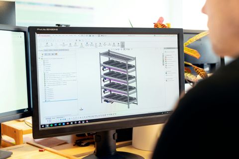 Person designs a structure on a computer screen. Gray 3D model of the rack. Office setting.