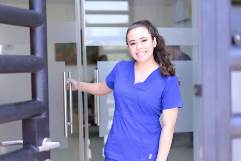 Woman in blue scrubs opening a door, smiling.