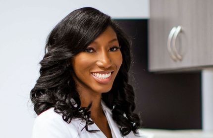 A woman in a white lab coat is smiling for the camera.