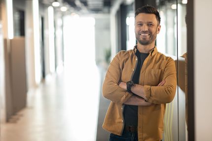 A man is standing in a hallway with his arms crossed and smiling.