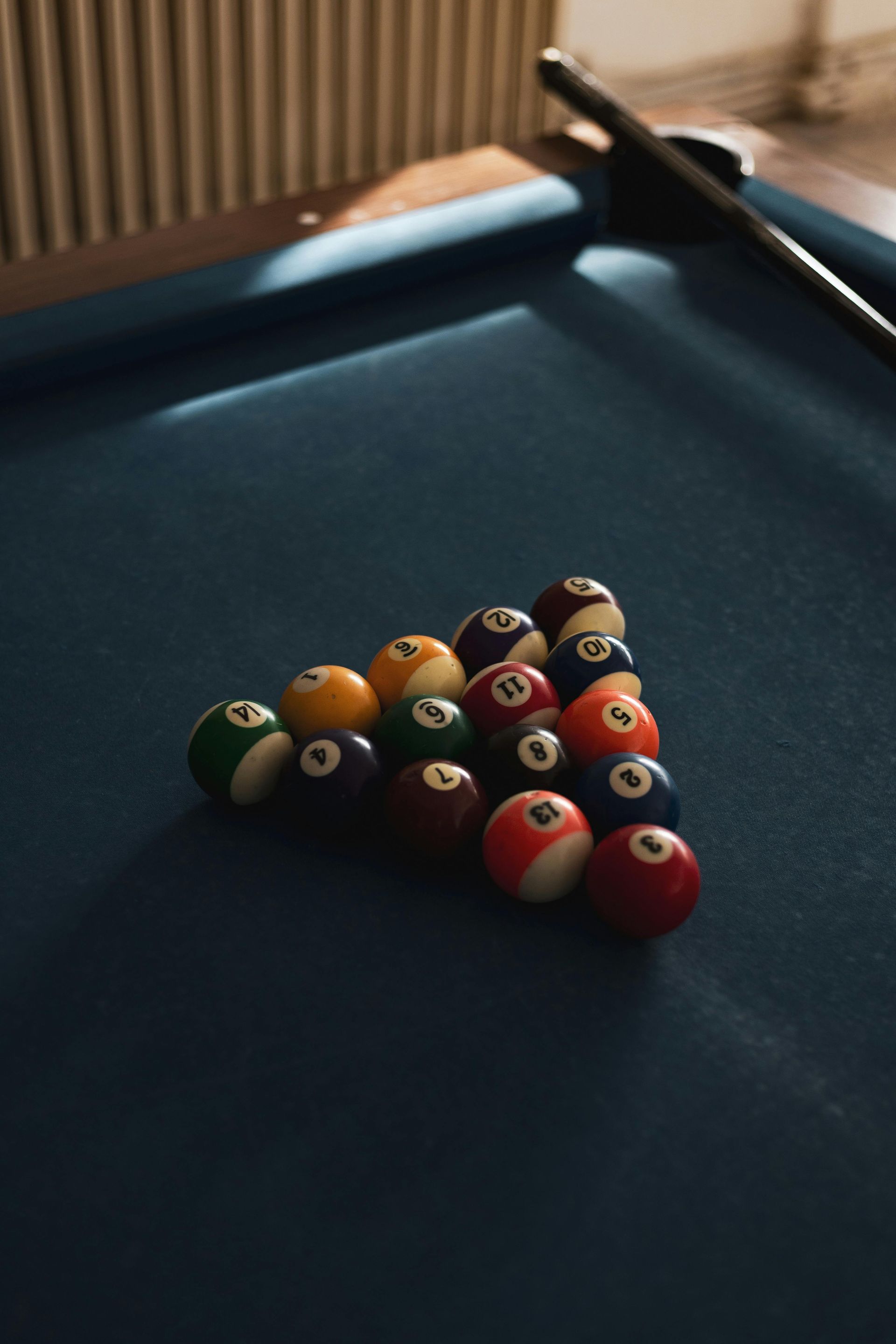 Pool balls racked in a triangle on a blue felt table, cue stick resting nearby.