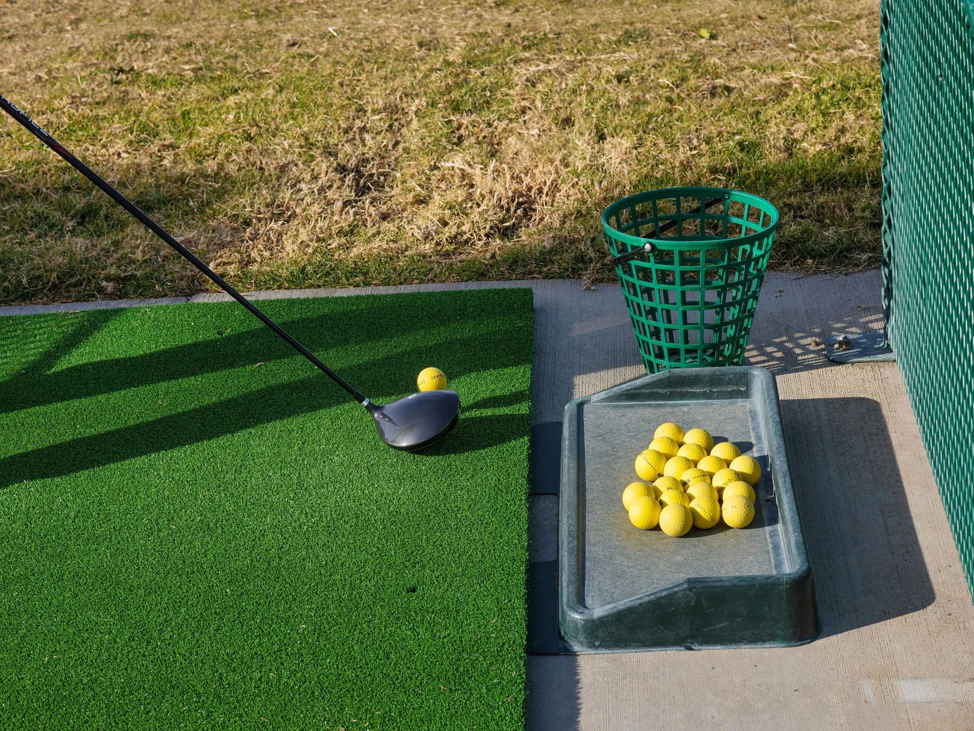 Close-up of a person striking golf balls at a driving range, with the club contacting the ball and others scattered on the practice mat.